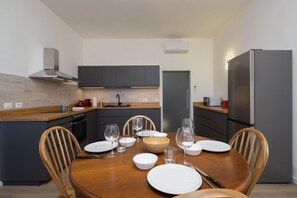 Una cocina moderna con armarios oscuros, una mesa de comedor de madera para cuatro comensales y un refrigerador de acero inoxidable.