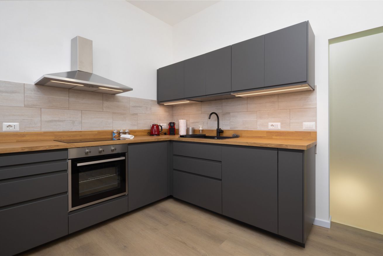 A modern kitchen with dark cabinetry, a wooden countertop, an oven, a stove, and a range hood.