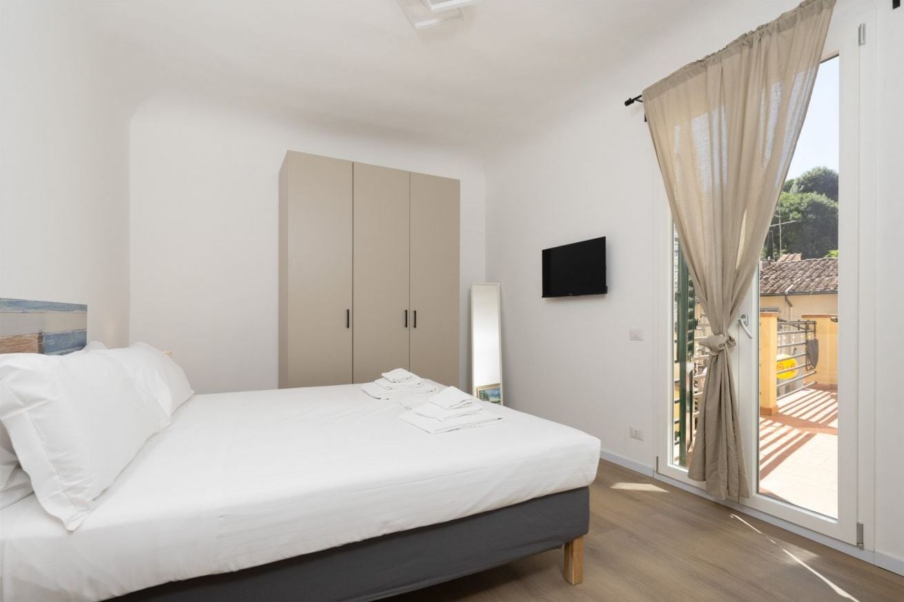 A bedroom with a bed, a wardrobe, a television, and a window with curtains.