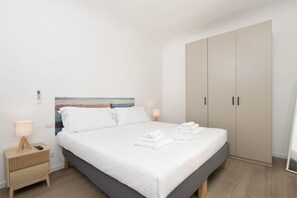 A neatly made bed with white linens, a bedside table with a lamp, and a wardrobe with two doors.