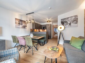 Uma sala de estar moderna com um sofá, cadeiras, uma mesa de jantar e uma cozinha ao fundo.