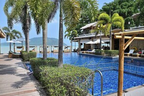 A poolside area with lounge chairs, a wooden deck, and a view of the sea. - Beachfront and Pool 2 BR Apt- Celeena 870 (Rawai)