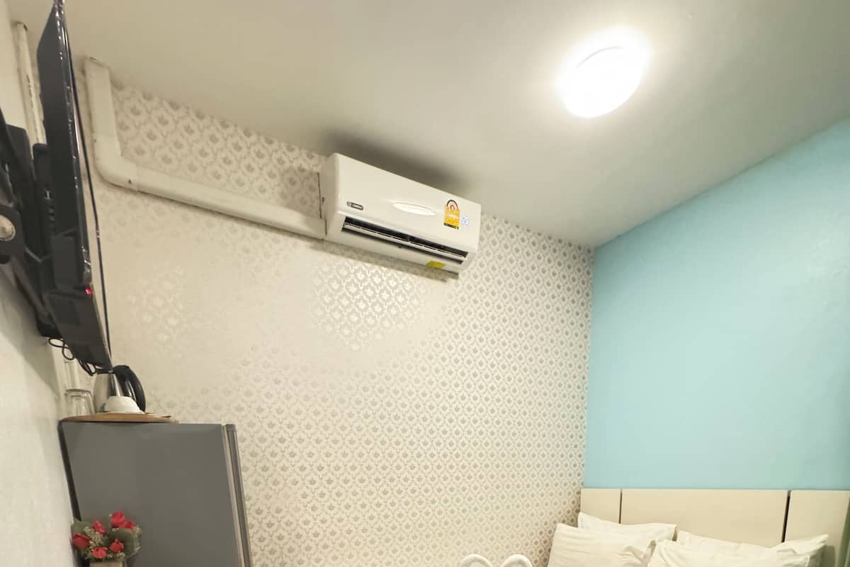 A hotel room with a bed, a desk, a TV, and an air conditioner.