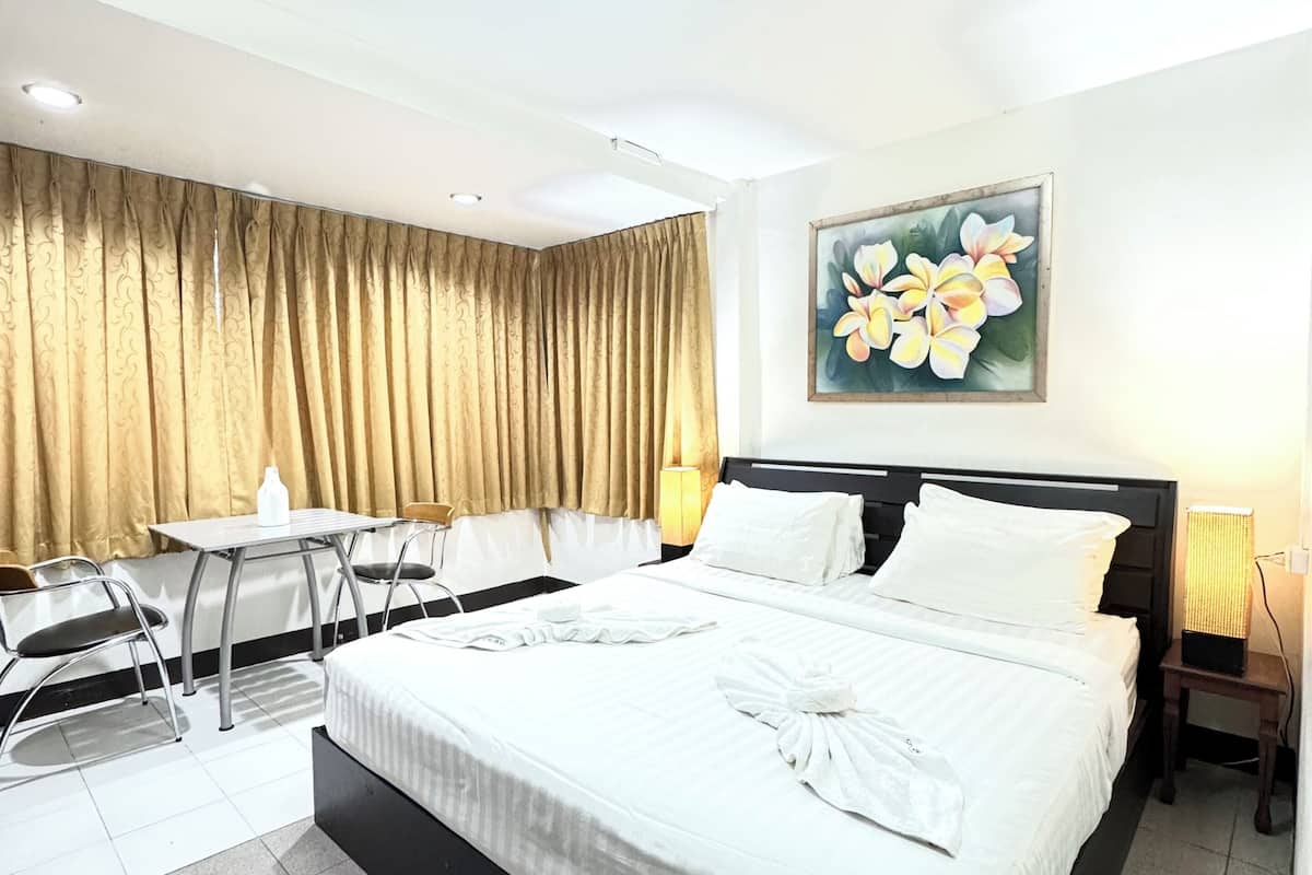 A hotel room with a large bed, a desk with chairs, a painting of flowers on the wall, and a ceiling light.