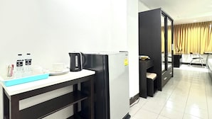 A hotel room with a kitchenette, a bed, a desk with a chair, and a window with curtains. - La Casa Residencies (Patong)