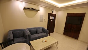 Una sala de estar con un sofá gris, una mesa de centro blanca y un televisor montado en la pared.