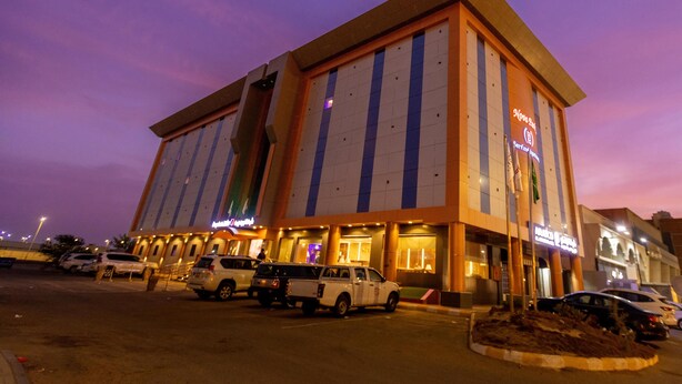 Un hotel con diseño arquitectónico moderno, que presenta una entrada destacada y un estacionamiento con varios vehículos.