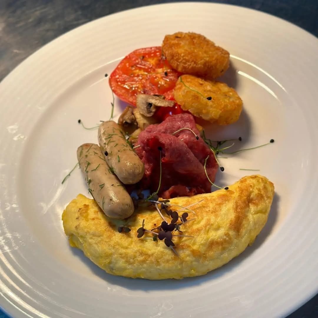Une assiette contenant une omelette, des tomates, des champignons et des saucisses.