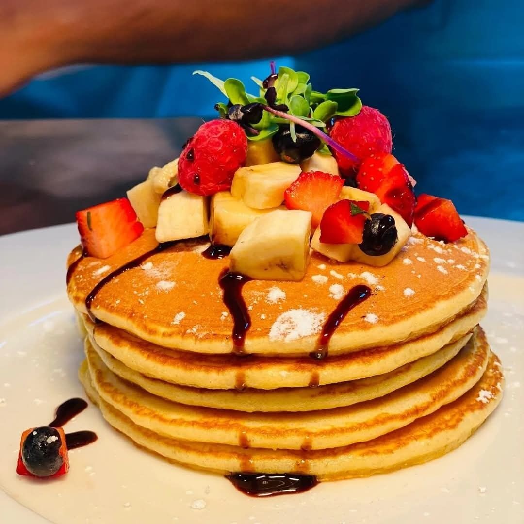 A stack of pancakes topped with fruit and syrup.