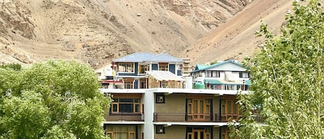 A multi-story building with balconies, surrounded by greenery and a mountainous backdrop.
