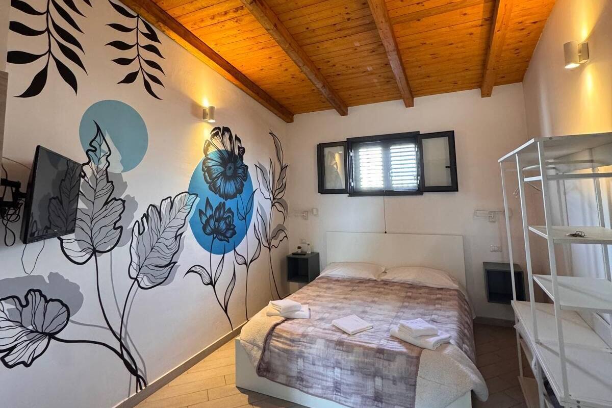 A bedroom with a wooden ceiling, a bed with a patterned bedspread, a wall with floral artwork, and a bunk bed to the right.