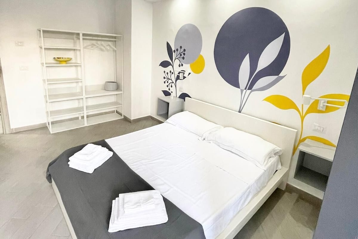 A modern hotel room with a large bed, a wardrobe, and a wall with a floral mural.