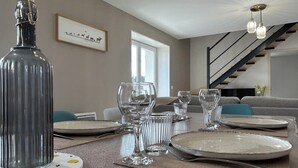 Un comedor con una mesa dispuesta para cuatro, una botella y un cuadro en la pared.