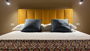 Une chambre d’hôtel avec un lit, deux oreillers, une couvre-lit à motifs, une tête de lit et deux lampes suspendues.