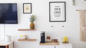 Una sala de estar moderna con un televisor de pantalla plana, obras de arte enmarcadas, una piña y un colgador de macramé.