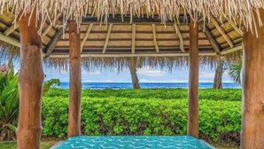 Un espacio al aire libre cubierto con piscina, pilares de madera y vista al océano.