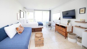 Una habitación moderna y luminosa con un sofá azul, un aparador de madera, un televisor y una mesita pequeña.