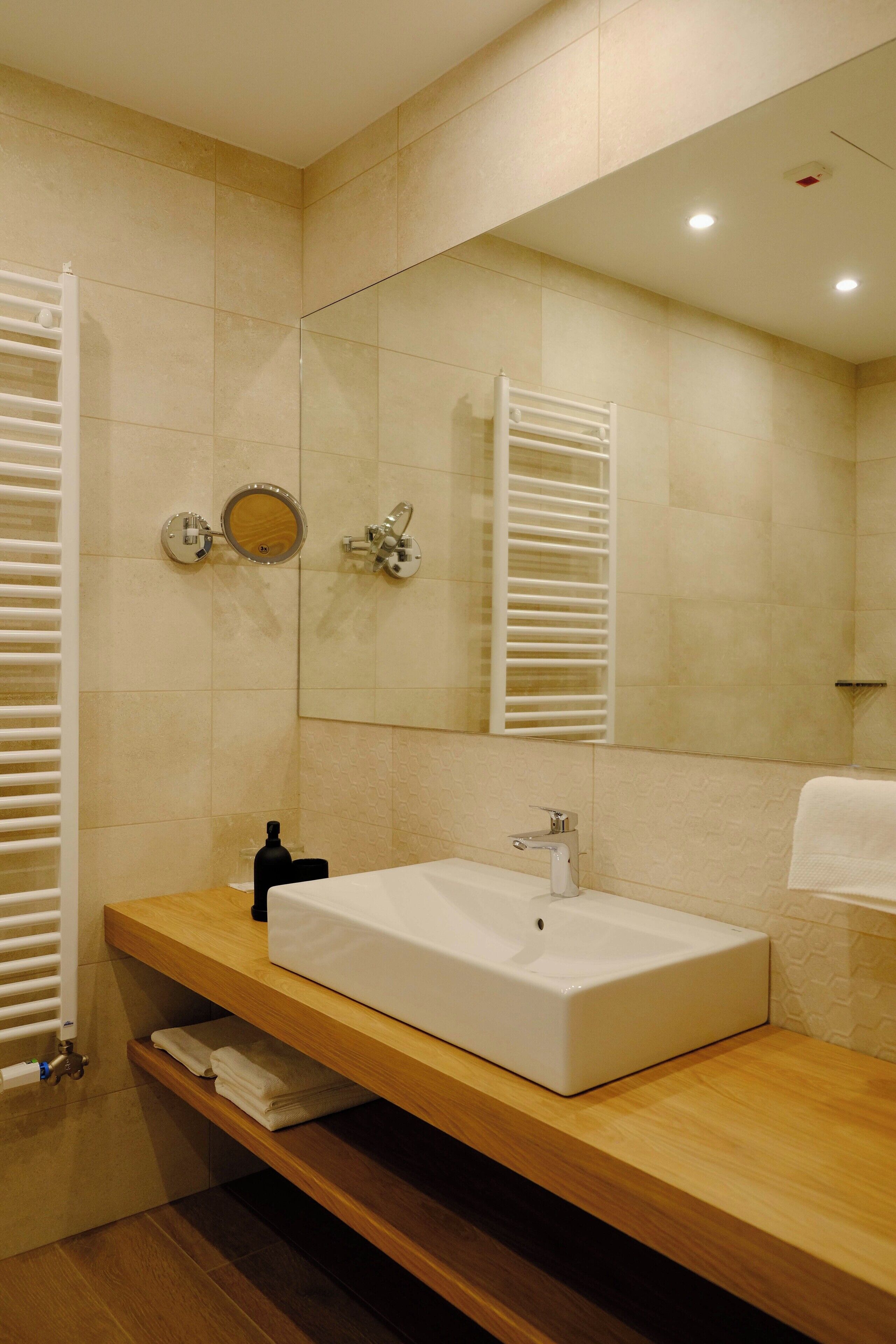 A bathroom with a white sink, wooden vanity, towel rack, and a large mirror.
