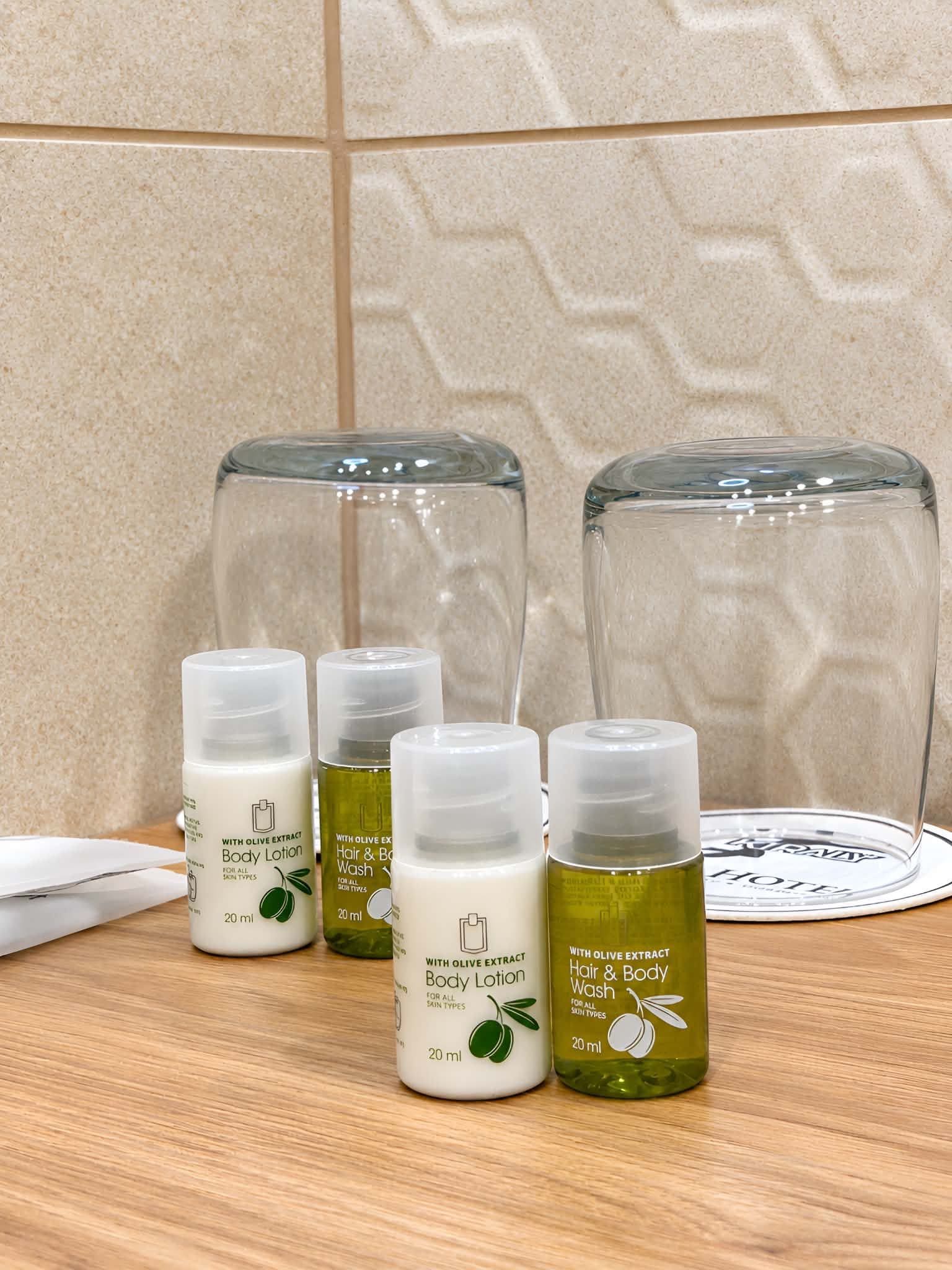 Baño con encimera de madera, toalla blanca y cuatro botellas de loción corporal y crema para cabello y cuerpo.