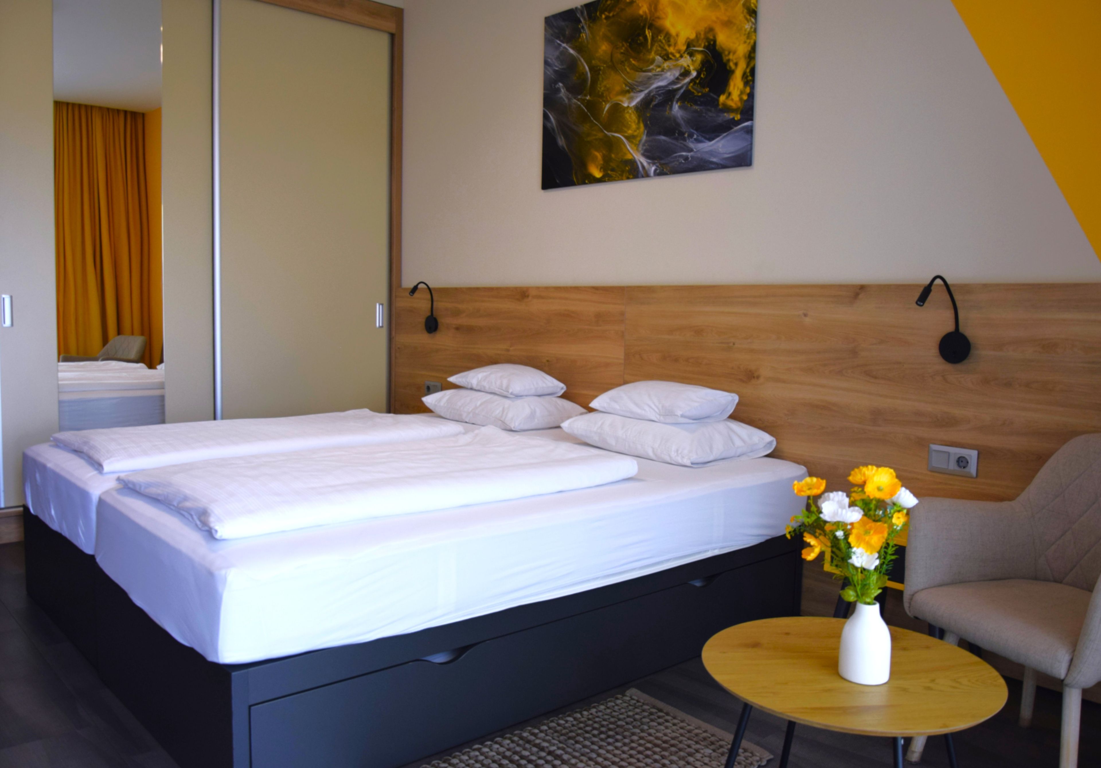 Una camera d'albergo con un letto, un comodino con un vaso di fiori e una sedia.