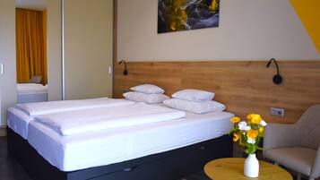 Una camera d'albergo con un letto, un comodino con un vaso di fiori e una sedia.