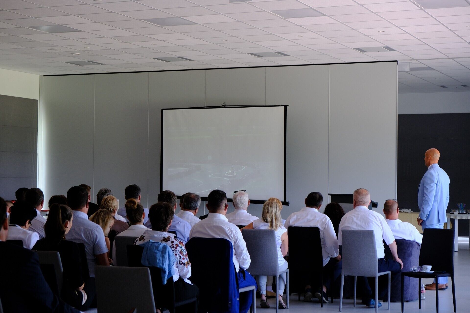 A conference room with a whiteboard, seated attendees, and a presenter.