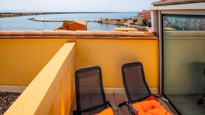 Un balcon avec deux chaises et une porte vitrée, donnant sur une étendue d’eau et une zone côtière.