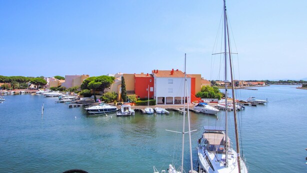 Un port de plaisance avec des bateaux amarrés, un bâtiment à la façade rouge et un ciel dégagé.