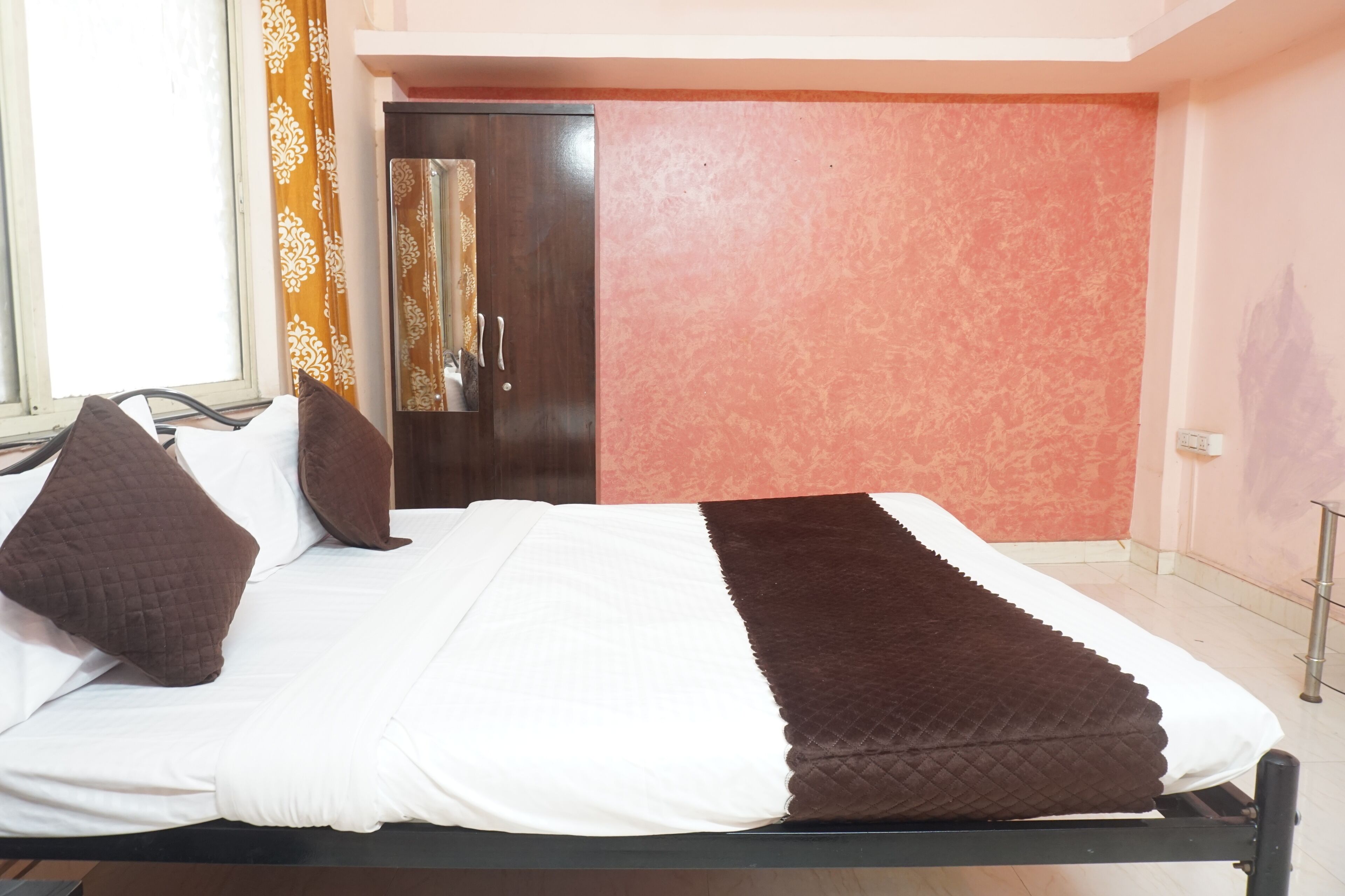 A neatly made bed with white and brown bedding, a wooden headboard, and a red textured wall.