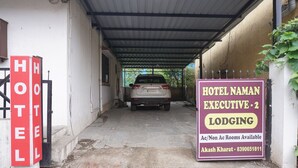 Un área de estacionamiento techada con un letrero que indica Hotel Naman Executive - 2 Lodging, mostrando habitaciones disponibles e información de contacto.