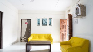 Una habitación con un sofá amarillo, una mesa de centro de madera y cuadros en la pared.