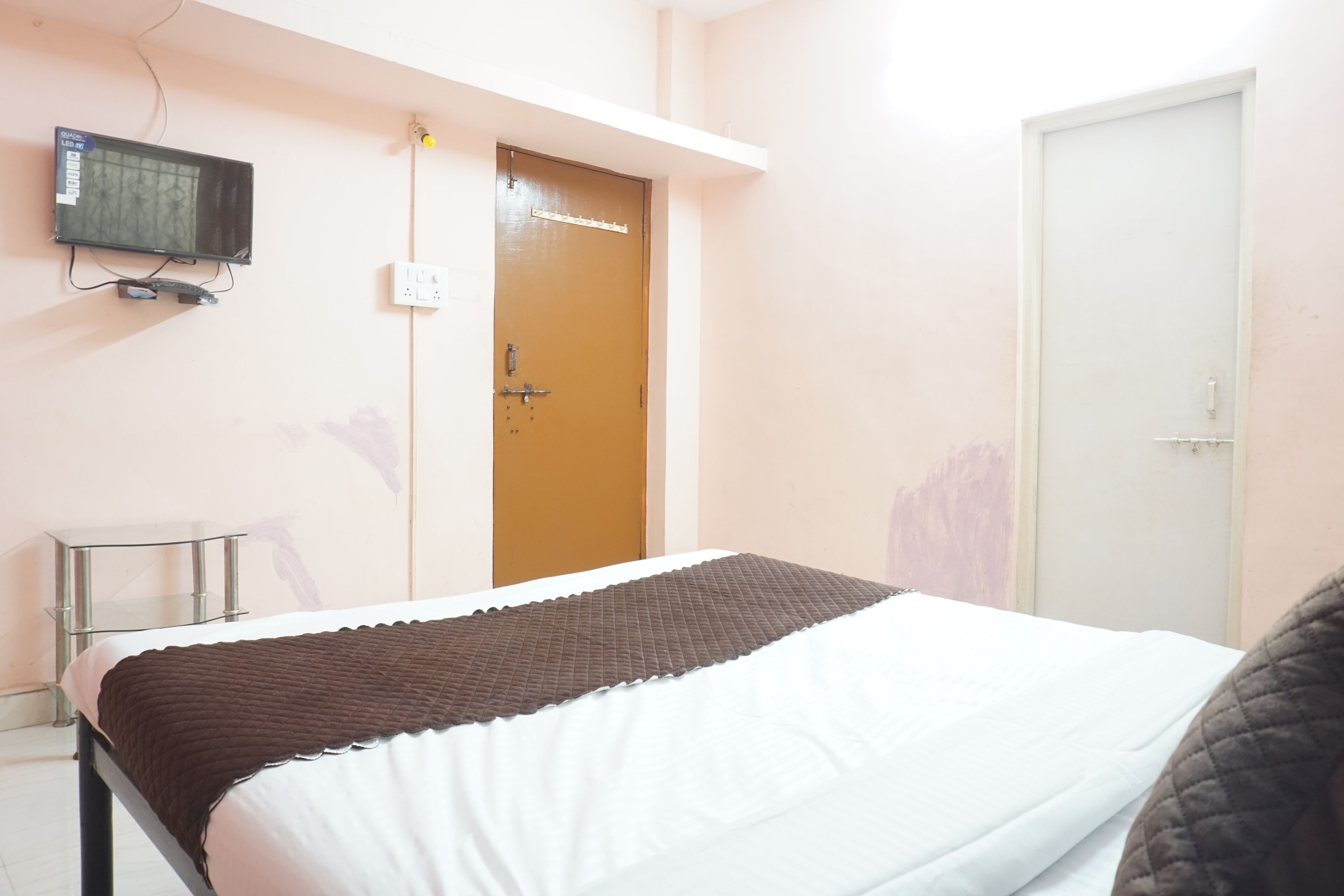 A bedroom with a bed, a television mounted on the wall, a door, and a small table.