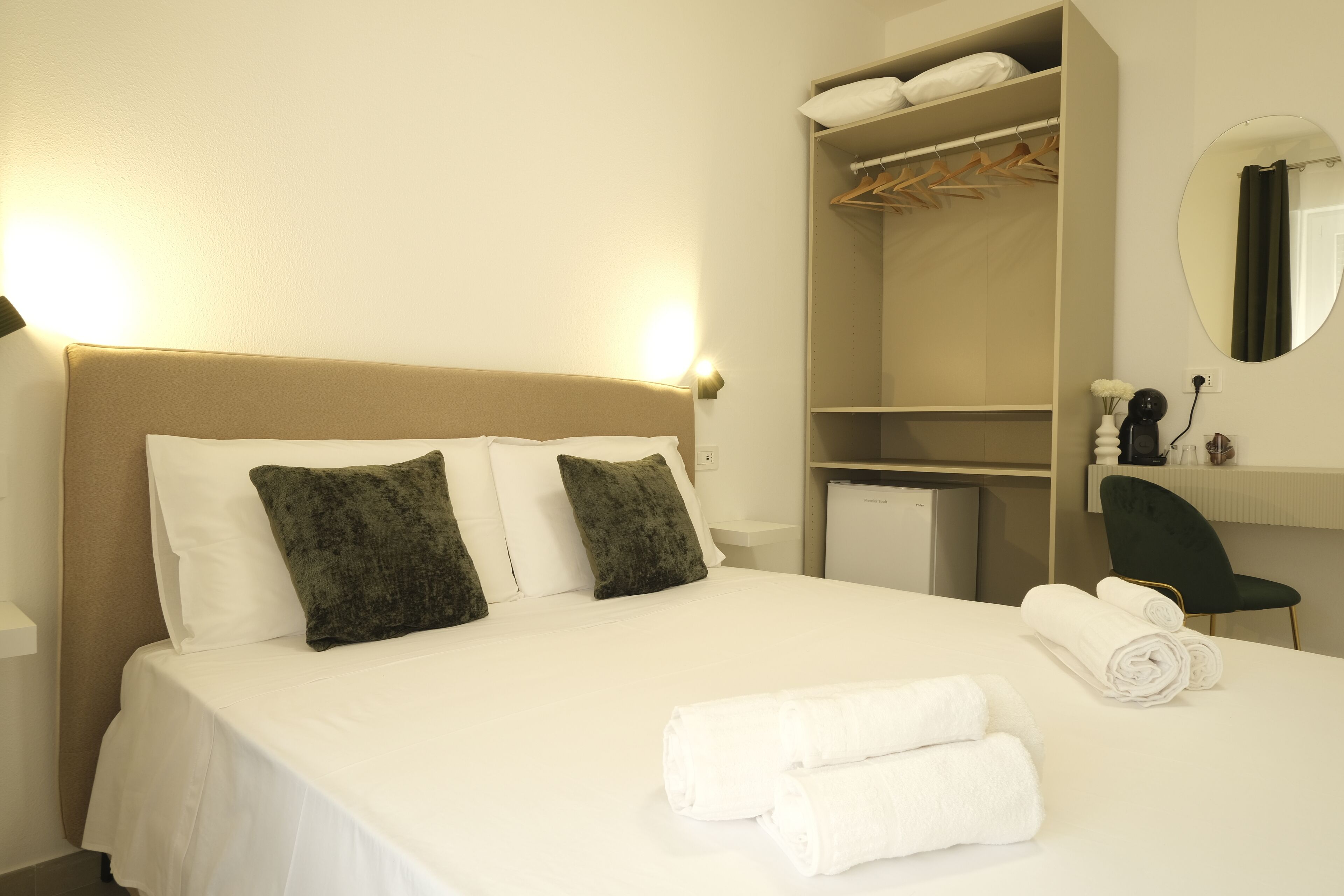 A hotel room with a bed, a wardrobe, a mirror, and a desk with a chair.