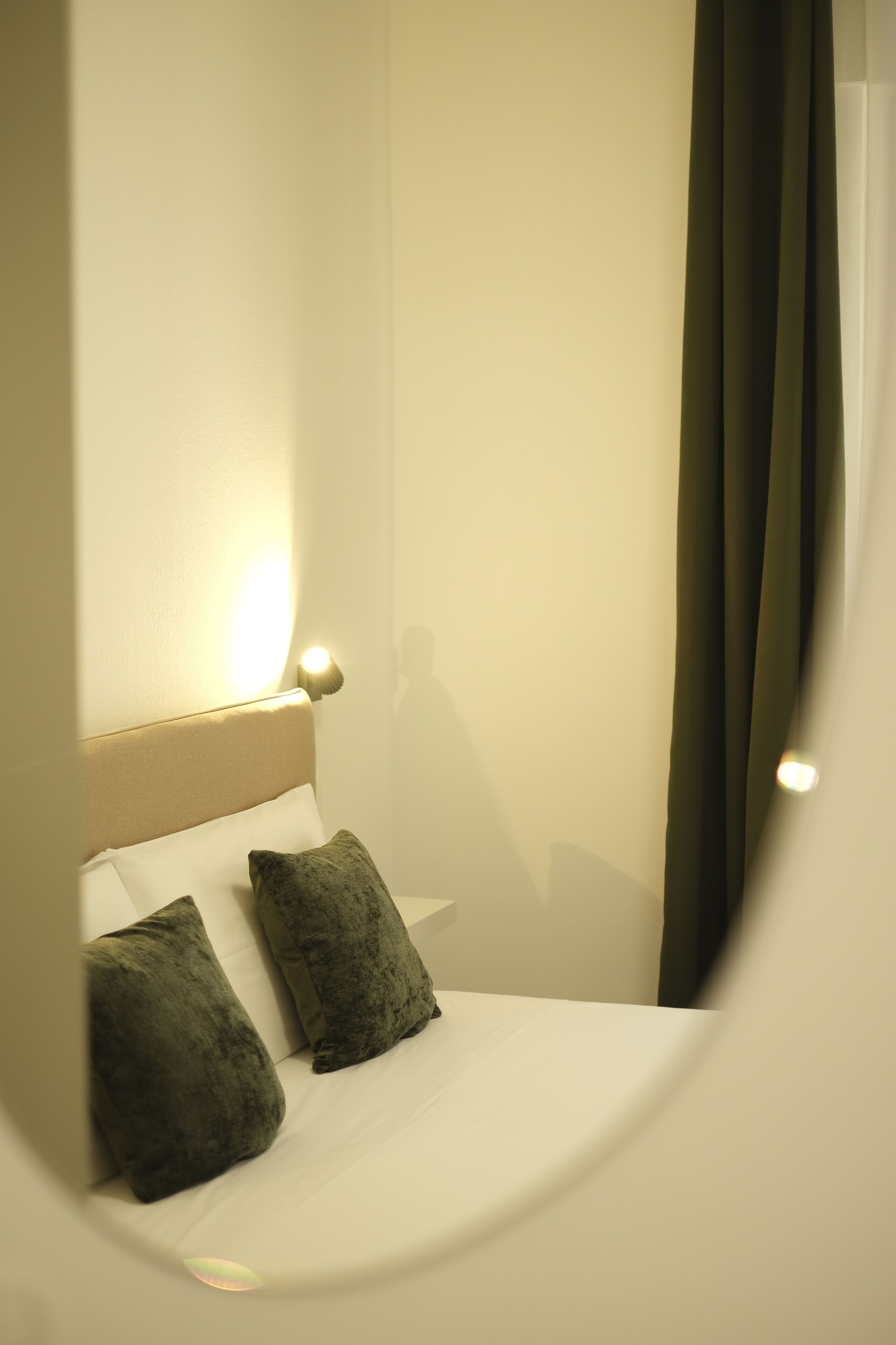 A neatly made bed with two pillows, a headboard with a light fixture, and a view of a curtain.