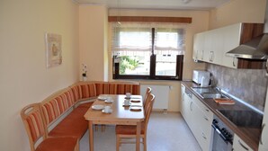 Une cuisine avec un coin repas, comprenant une table et des bancs, une fenêtre avec des stores et une cuisinière.