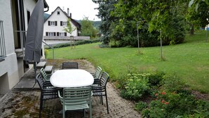 Une terrasse avec une table et des chaises, un parasol et un jardin agrémenté de diverses plantes et fleurs.