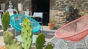 A stone building with a door and windows, a cactus in the foreground, and two chairs. - Villa Medena (Mayenne)