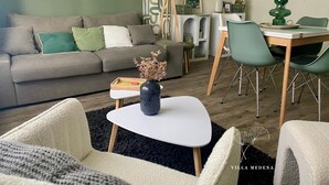A modern living room with a grey sofa, green cushions, a white coffee table, and a dining area with green chairs and a white table. - Villa Medena (Mayenne)