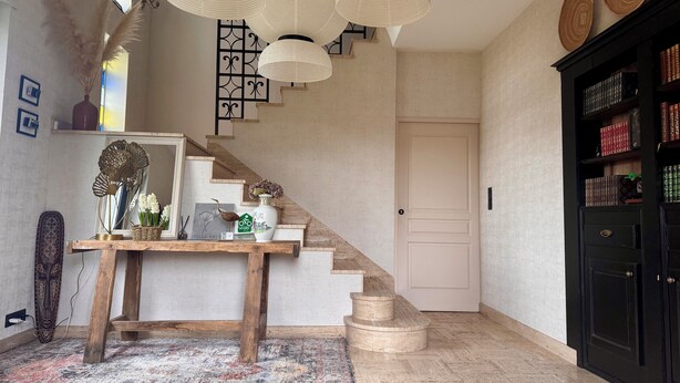 A staircase with a white door at the top, a wooden table with decorative items, and a black bookshelf with books. - Villa Medena (Mayenne)