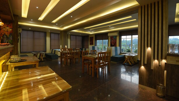 A spacious dining area with multiple tables and chairs, a wooden floor, and a view of the outdoors through large windows. - Hotel Lakefront (Ranchi)
