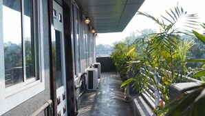 A covered balcony with potted plants, large windows, and air conditioning units. - Hotel Lakefront (Ranchi)