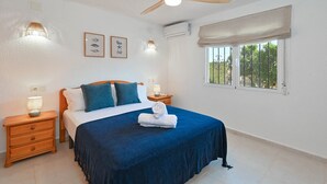 Ein Schlafzimmer mit einem Bett, Holz-Nachttischen, einem Deckenventilator, Wandleuchten, einem Fenster mit Blick und einem gerahmten Bild an der Wand.