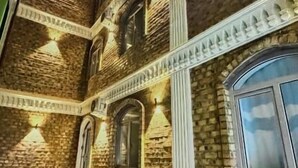 A multi-story building with a brick facade and white decorative trim. There are multiple windows, some with curtains, and a set of stairs leading to the entrance. - Siab Boutique Hotel (Samarkand)