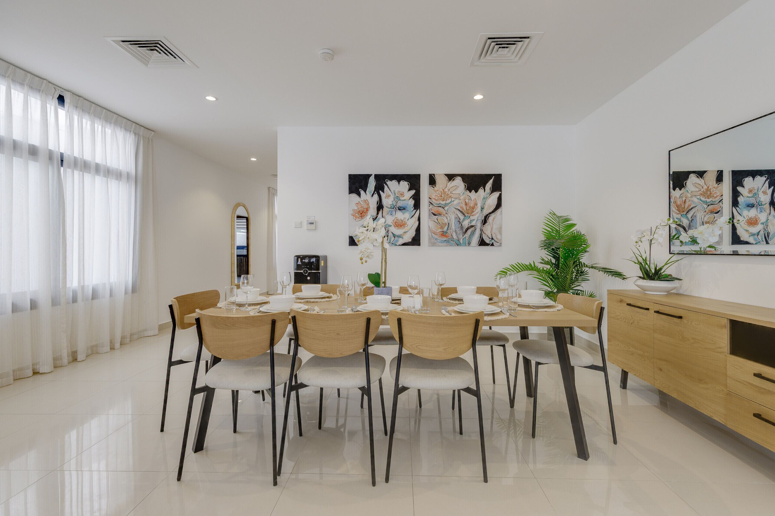 Un comedor moderno con una mesa larga preparada para seis personas, rodeada de sillas de madera.