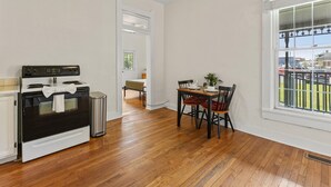 A kitchen with a stove, a trash can, and a dining area with a table and chairs. - Simple Comfort  1 Bed 1 Bath Near Downtown Indy (Indianapolis)
