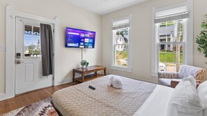 A hotel room with a bed, a TV mounted on the wall, a small table with a plant, and a view of the outside through a window. - Simple Comfort  1 Bed 1 Bath Near Downtown Indy (Indianapolis)