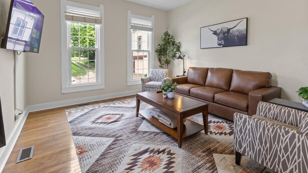 A living room with a brown leather sofa, patterned armchairs, a coffee table, and a TV mounted on the wall. - Simple Comfort  1 Bed 1 Bath Near Downtown Indy (Indianapolis)