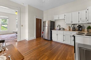 A modern kitchen with white cabinets, stainless steel appliances, and a wooden floor. - Simple Comfort  1 Bed 1 Bath Near Downtown Indy (Indianapolis)
