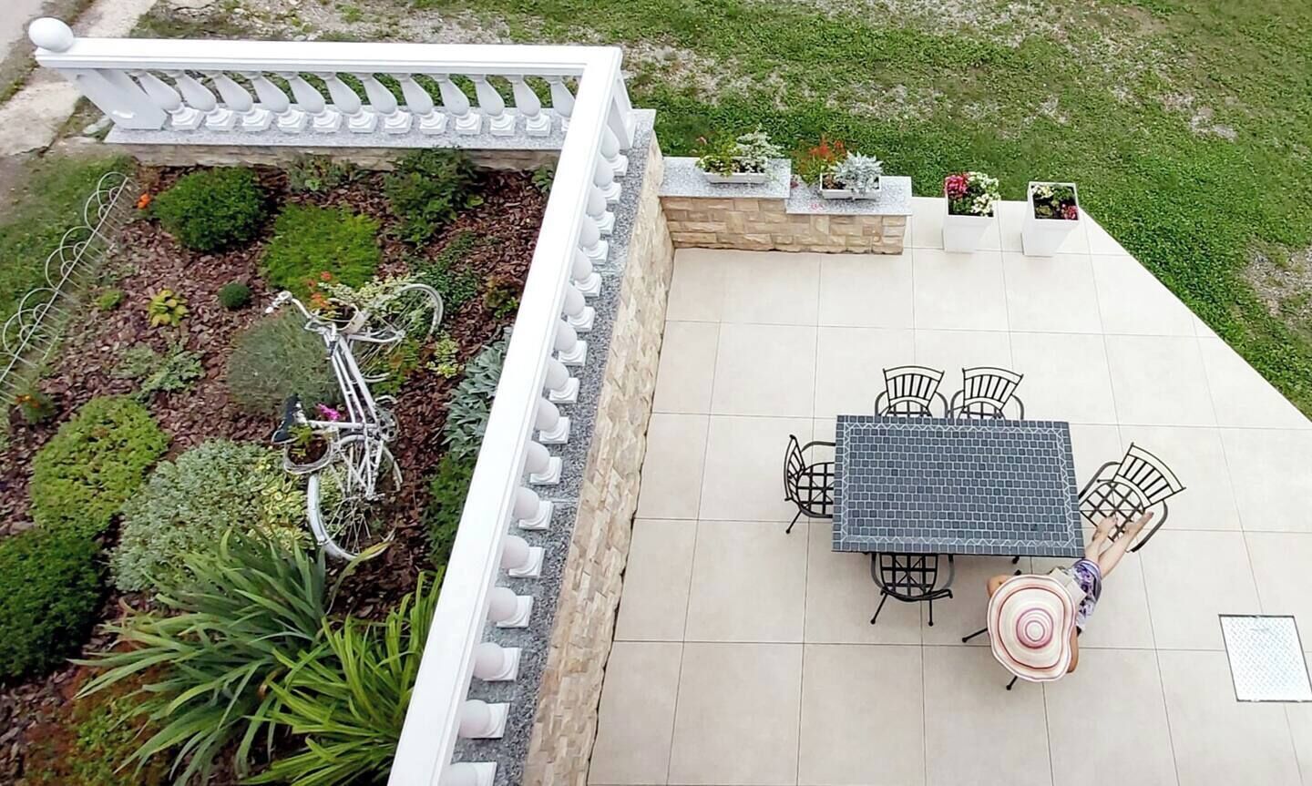 Un patio con una mesa y sillas, rodeado de plantas en macetas y una barandilla blanca.