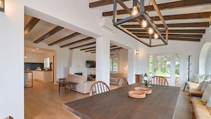 Ein großzügiger Essbereich mit einem großen Holztisch, Holzbalken an der Decke und Blick auf die Küche und den Wohnbereich im Hintergrund.